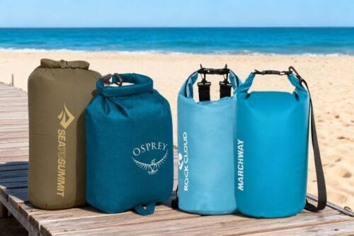 Four of the best dry bags — durable waterproof bags from Sea to Summit, Osprey, Rock Cloud, and Marchway displayed on a wooden dock by the beach.