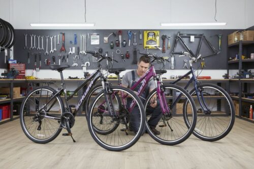 Professional bicycle mechanic examining three different hybrid bikes on display in a well-equipped workshop, showcasing the top models perfect for urban commuting and recreational cycling adventures.